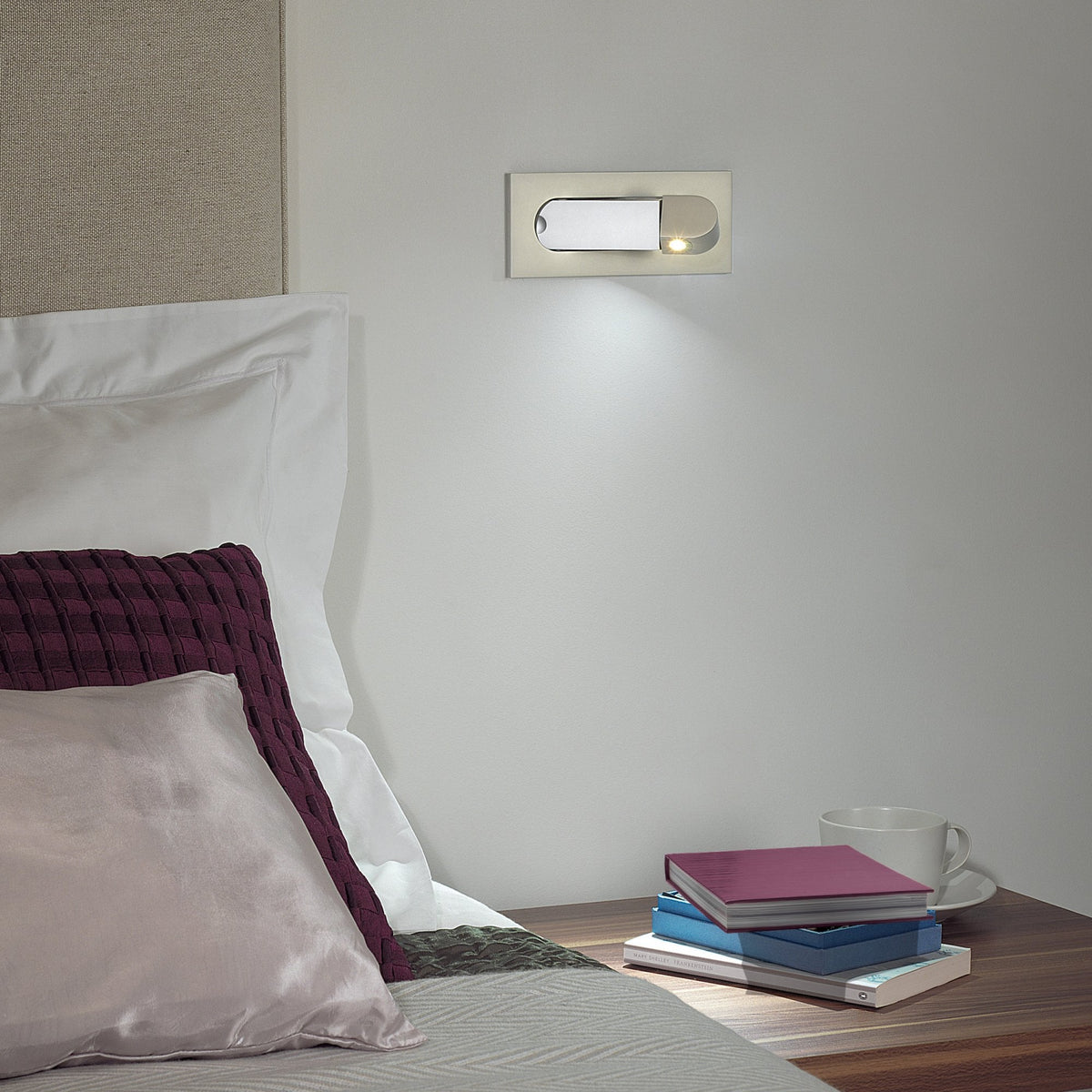 Wall-mounted reading light above a bedside table with books and a mug