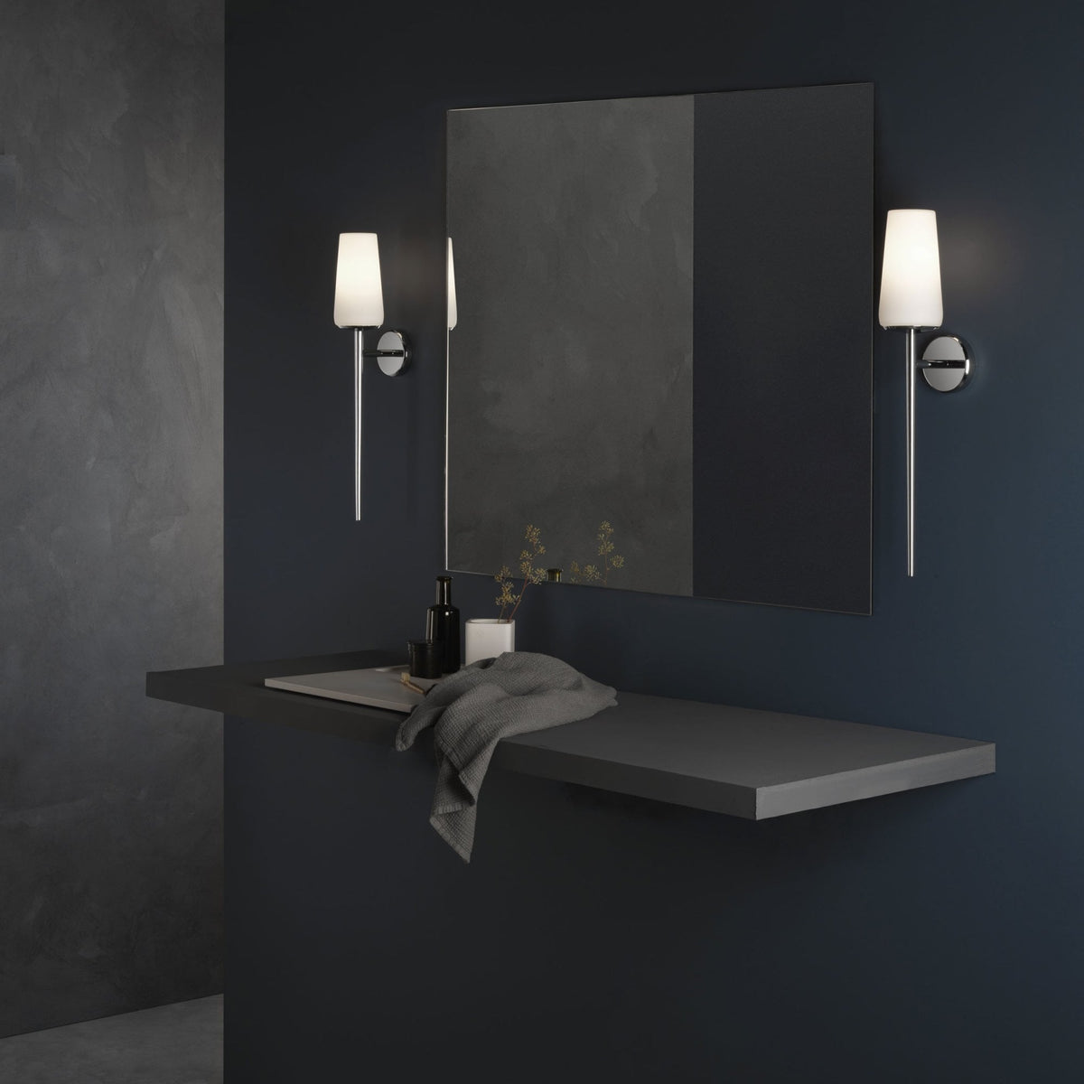 Bathroom with dark blue walls, a floating shelf, a mirror, and two wall-mounted lights