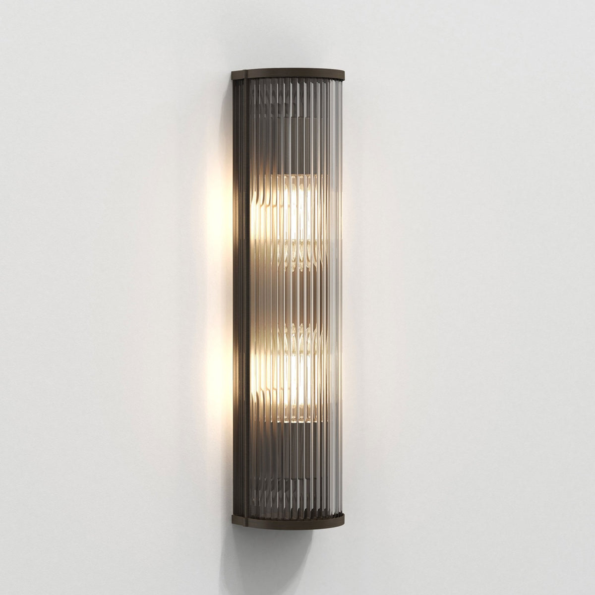 Vertical fluted glass wall light with a dark bronze frame, illuminated on a white wall