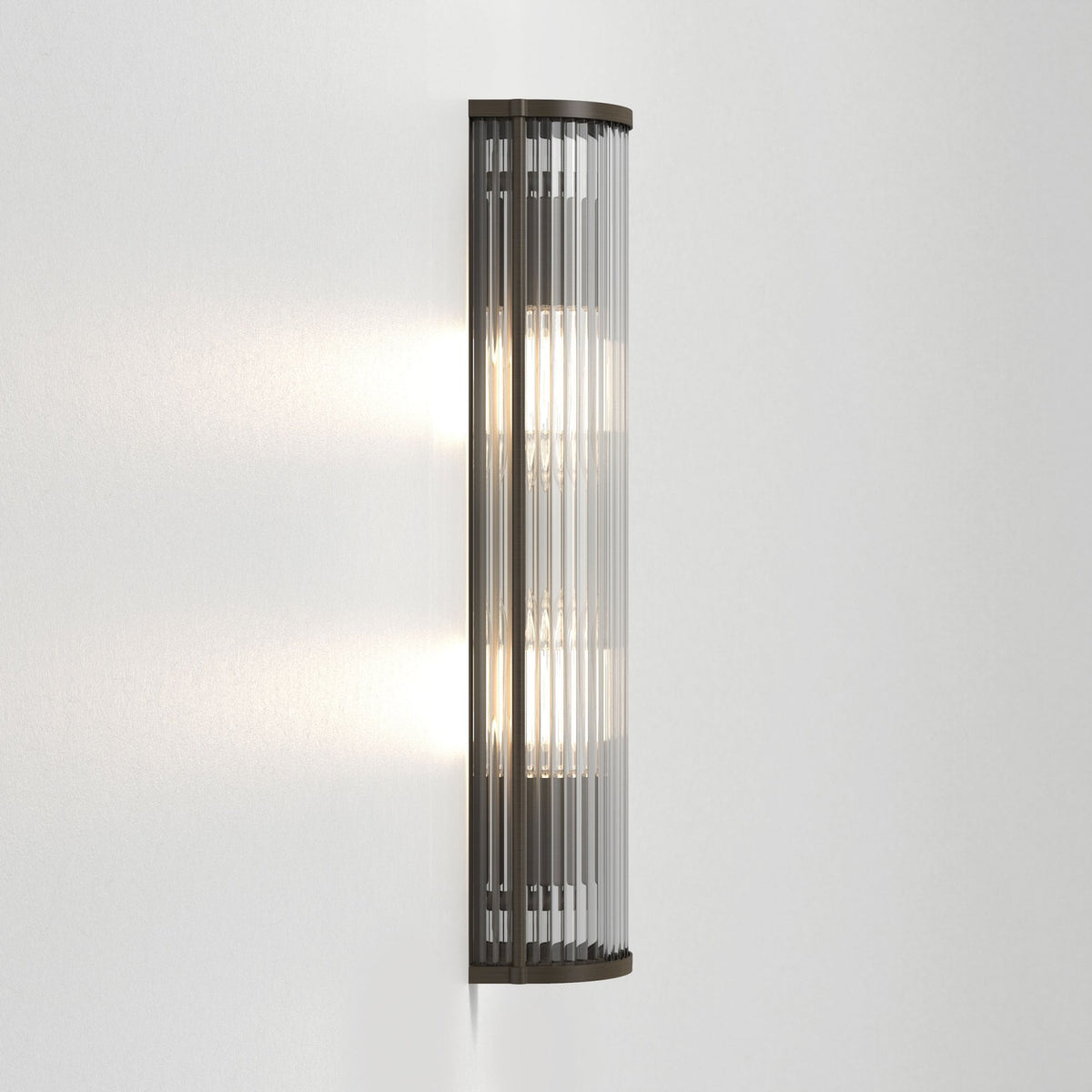 Tall wall light with a dark bronze frame and vertical clear glass rods, illuminated on a white wall