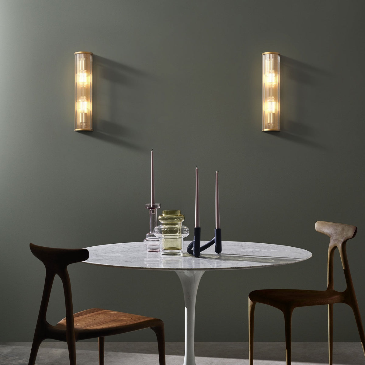Two wooden chairs at a marble table with candles and two vertical wall sconces