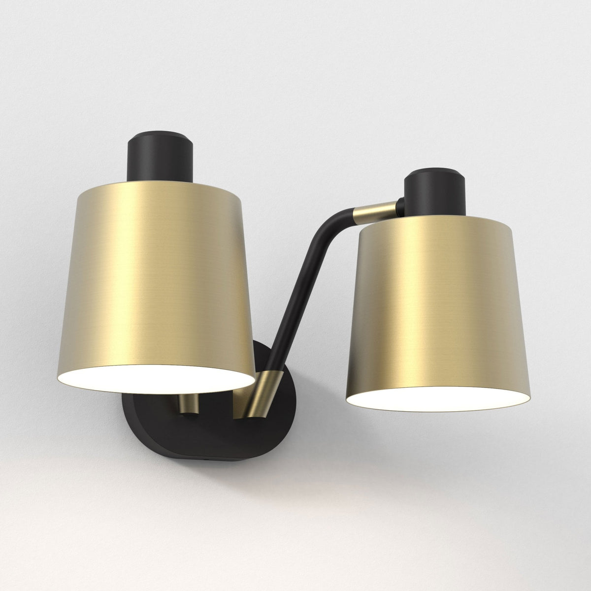 Two-light wall sconce with black base and curved arm, supporting two conical brass shades with illuminated interiors