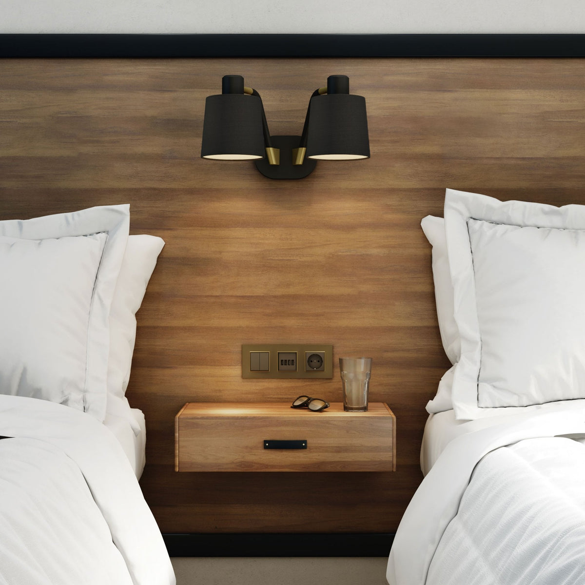 Two beds with white bedding and pillows, a wooden headboard, and a floating nightstand with a lamp