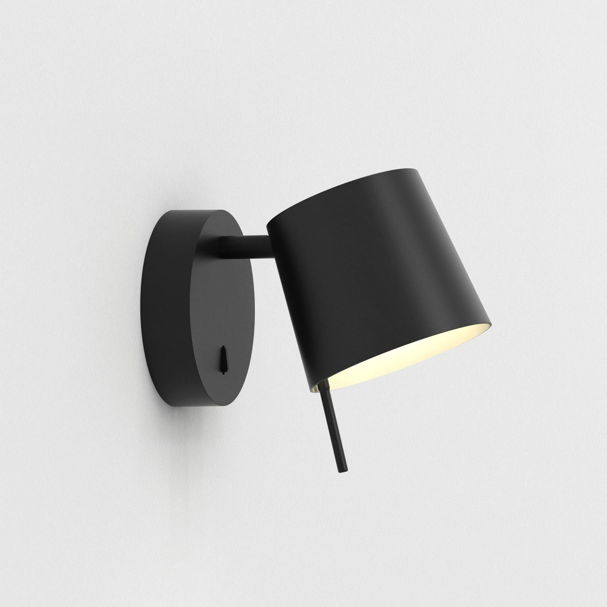 Black wall-mounted light fixture with a cylindrical shade angled downwards, emitting a warm glow