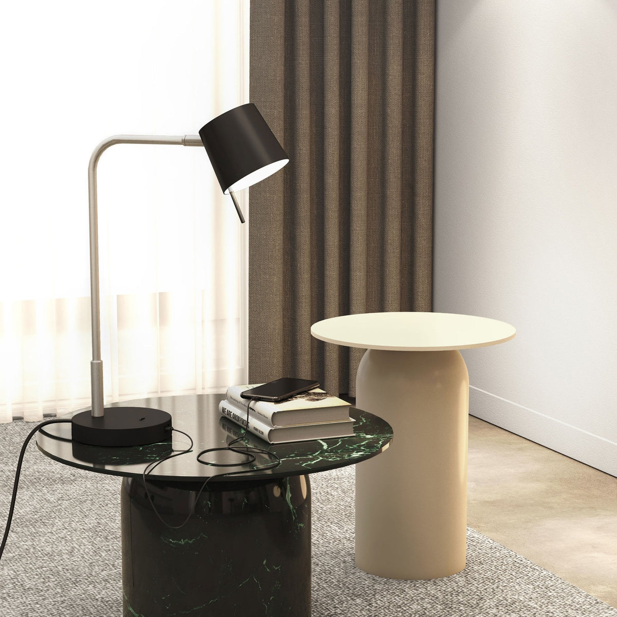 A black and silver desk lamp on a green marble table with books and a phone, next to a beige table