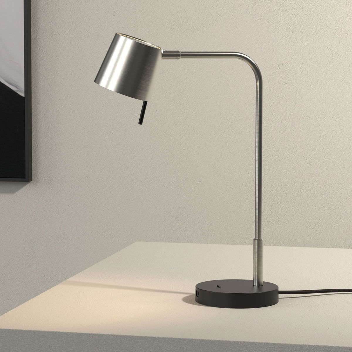 Brushed metal desk lamp with a black base and a curved arm, casting light onto a white surface
