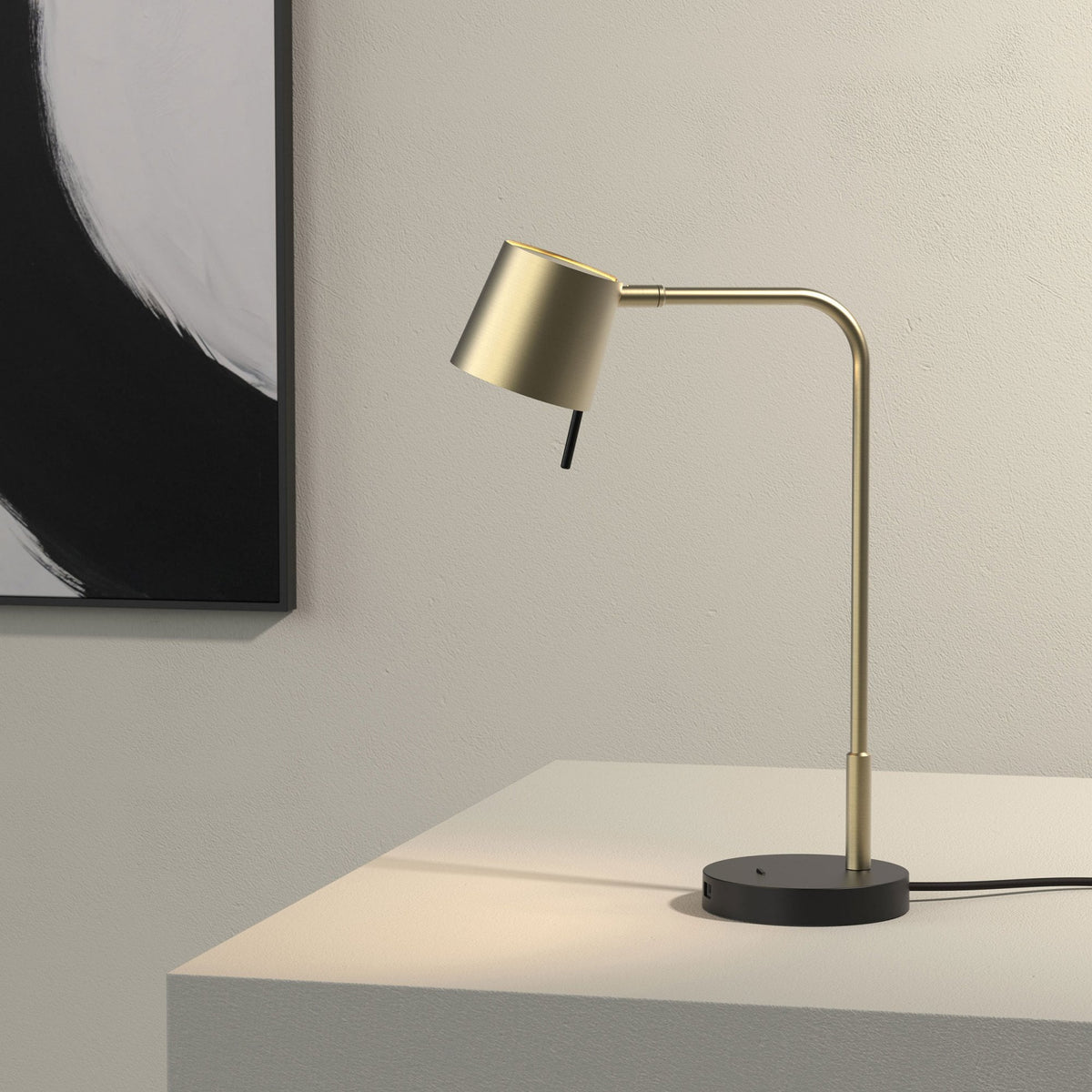 Brass desk lamp with a black base and a black and white abstract painting in the background