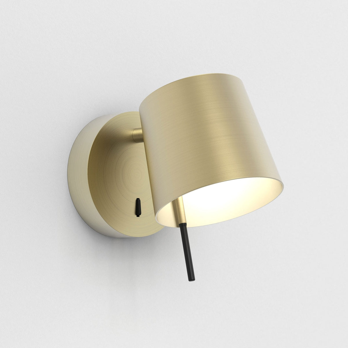 Brushed brass wall light with a conical shade and a black toggle switch on a white wall