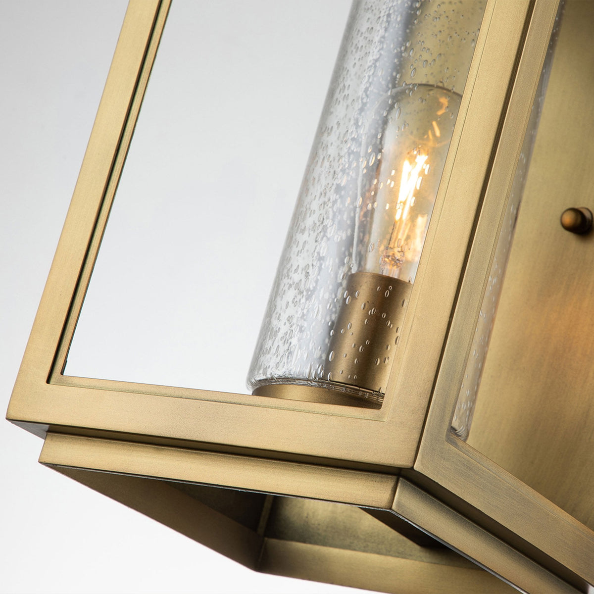 Angled view highlighting the base and seeded glass cylinder of the brass wall lantern.