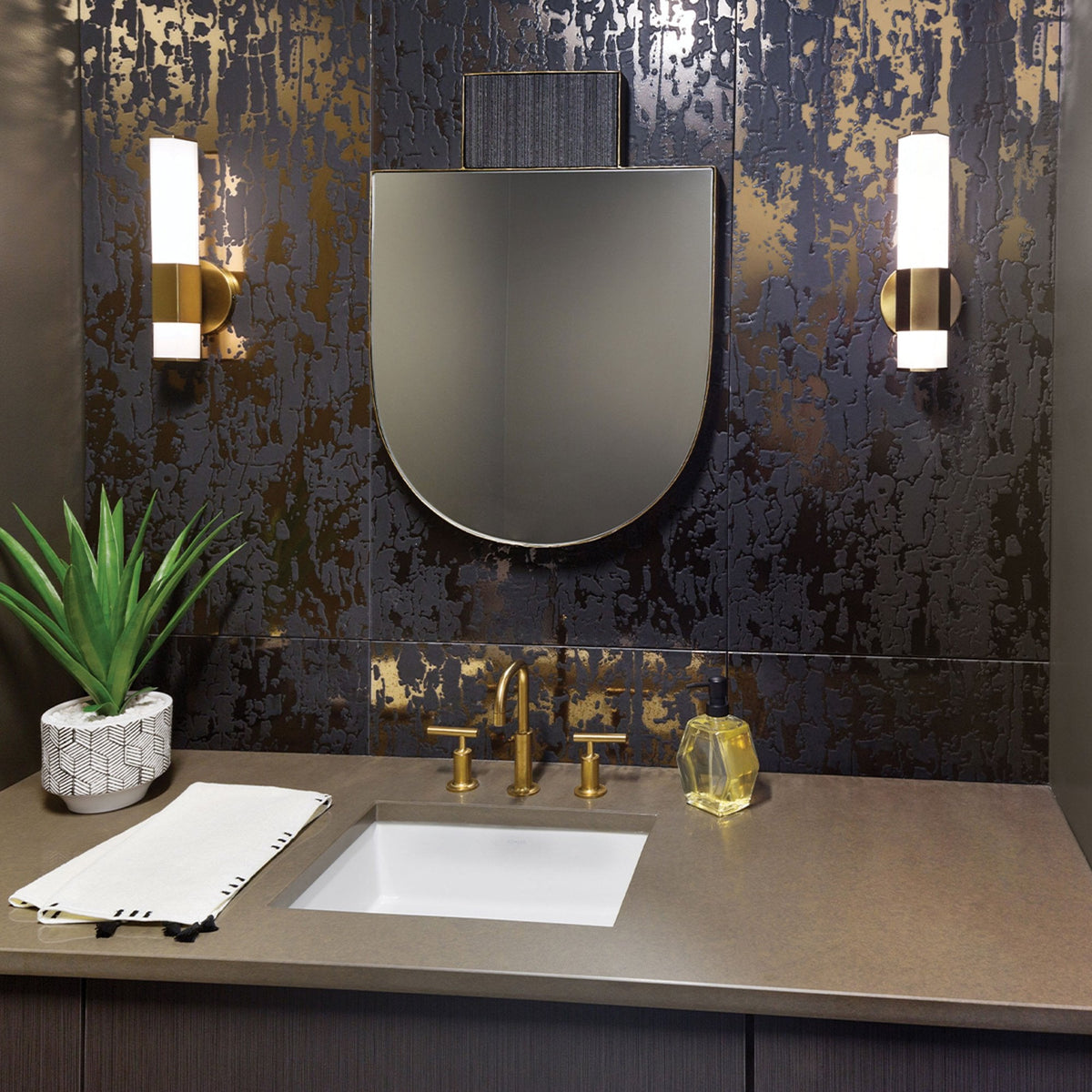A luxury bathroom featuring gold fixtures, a modern mirror, and a vibrant green plant.