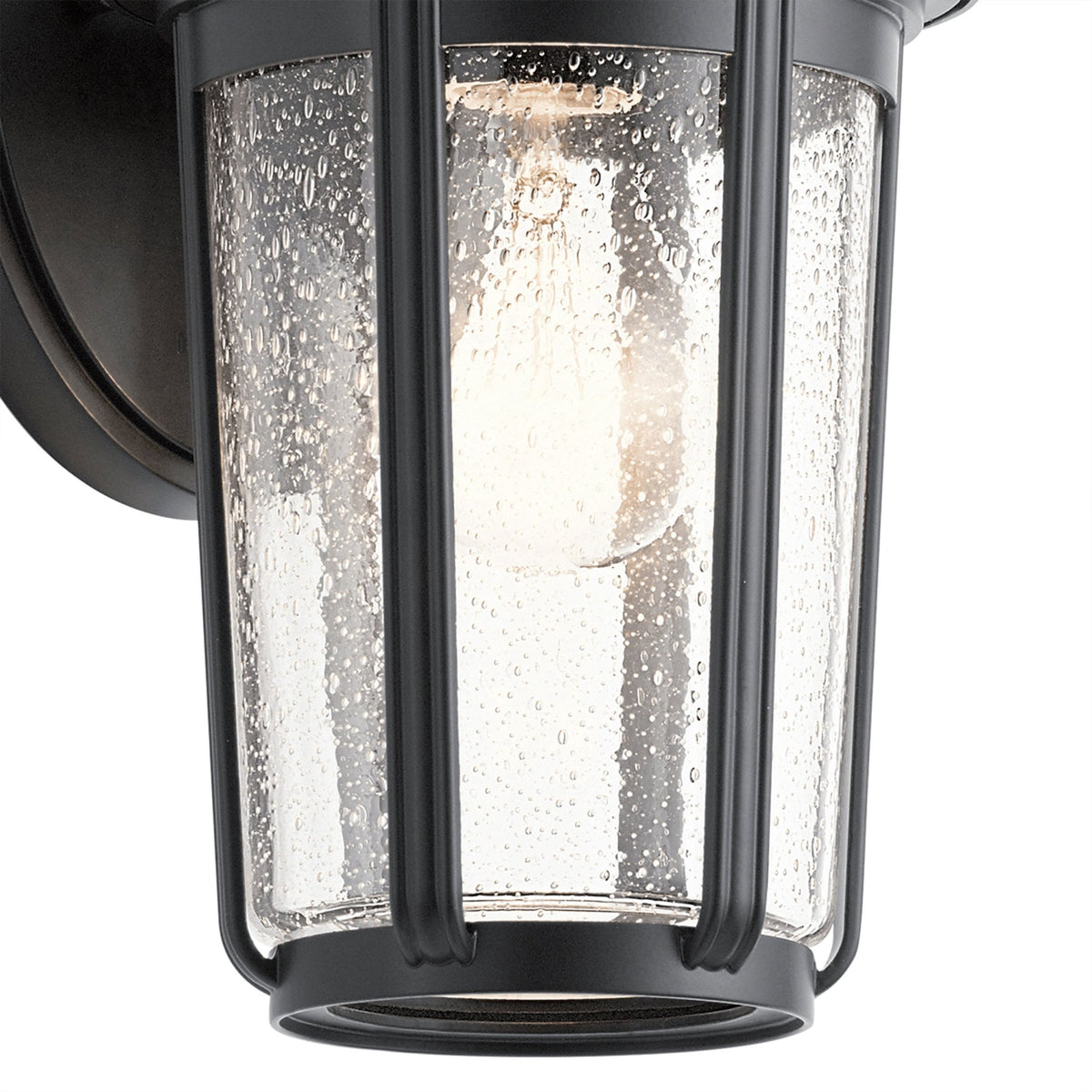 Close-up of the seeded glass shade and bulb of a black outdoor wall lantern.