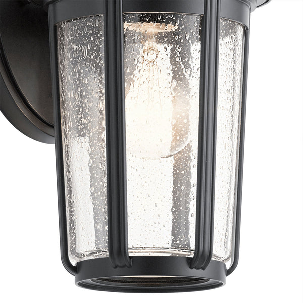 Close-up of the seeded glass shade and bulb of a black outdoor wall lantern.