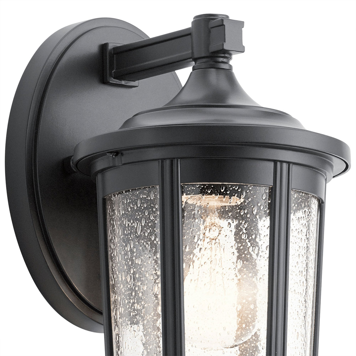 Top half of a black outdoor wall lantern, showing the arm, fixture, and seeded glass.