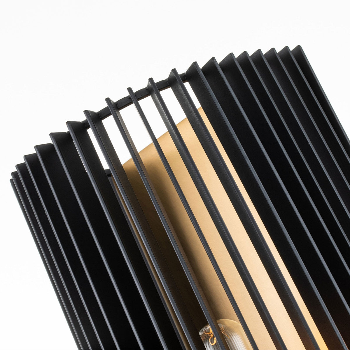 A close-up reveals the black slatted design and warm metallic interior of the wall sconce.