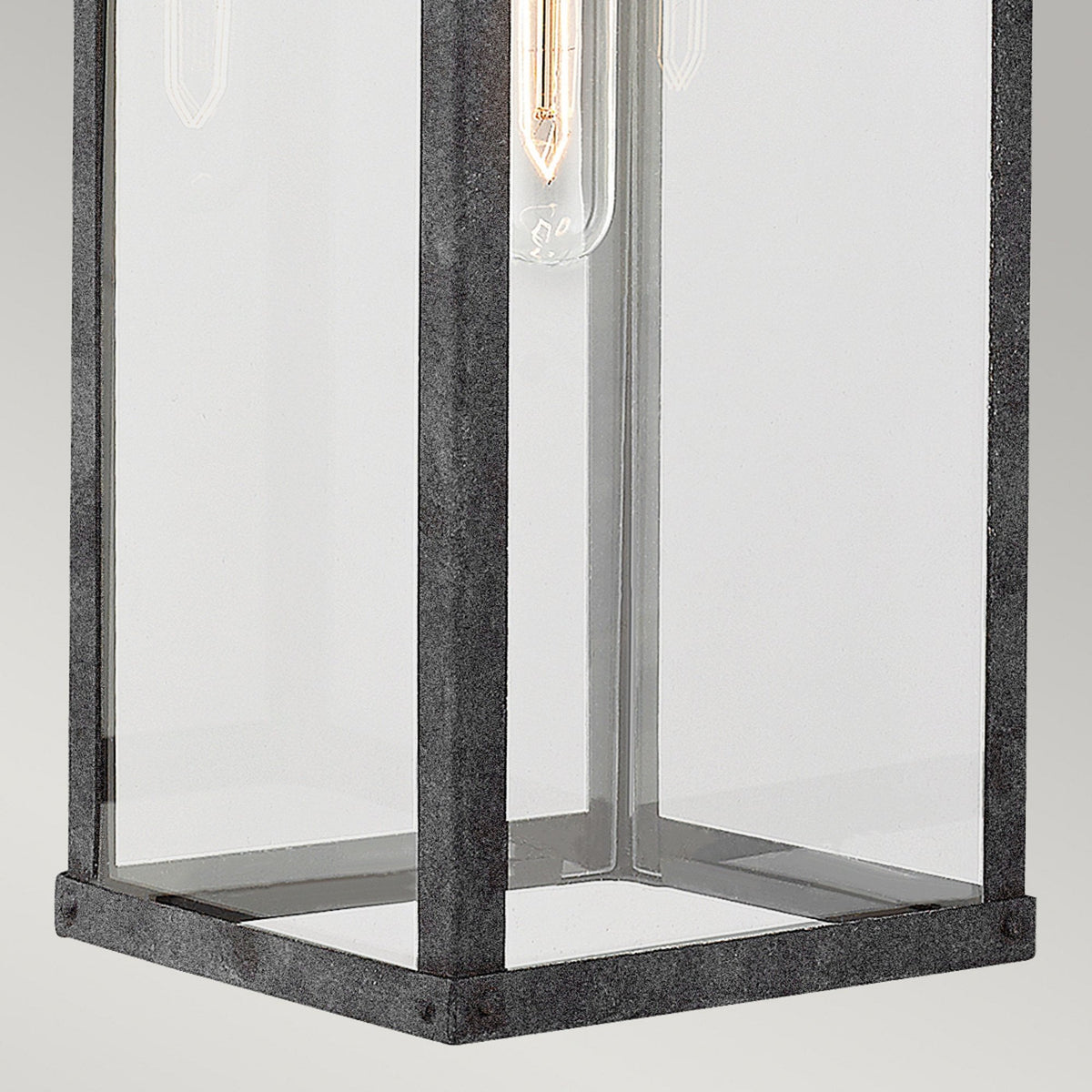 The base of the industrial wall light, showcasing the clear glass and dark metal frame.