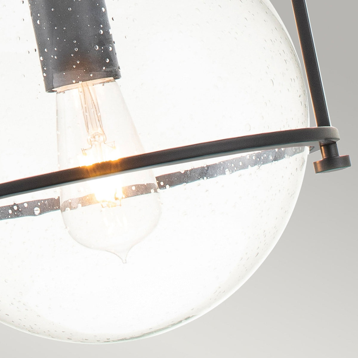 Detailed view of the light bulb inside the clear seeded glass shade of the pendant.