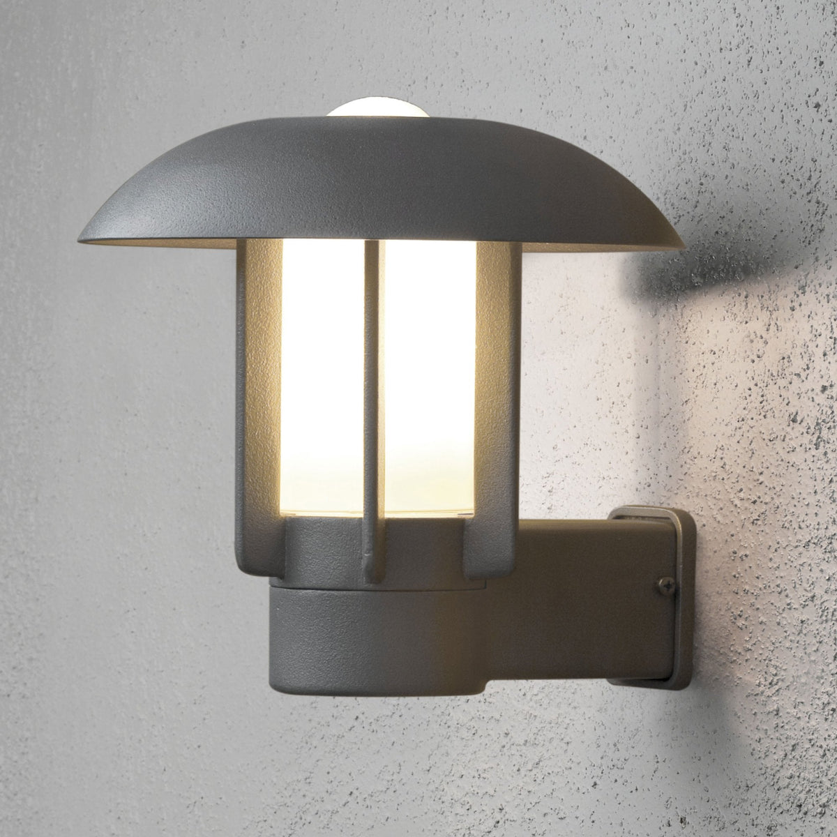 A modern outdoor wall light with a grey finish and a mushroom-shaped top, illuminating a textured wall.