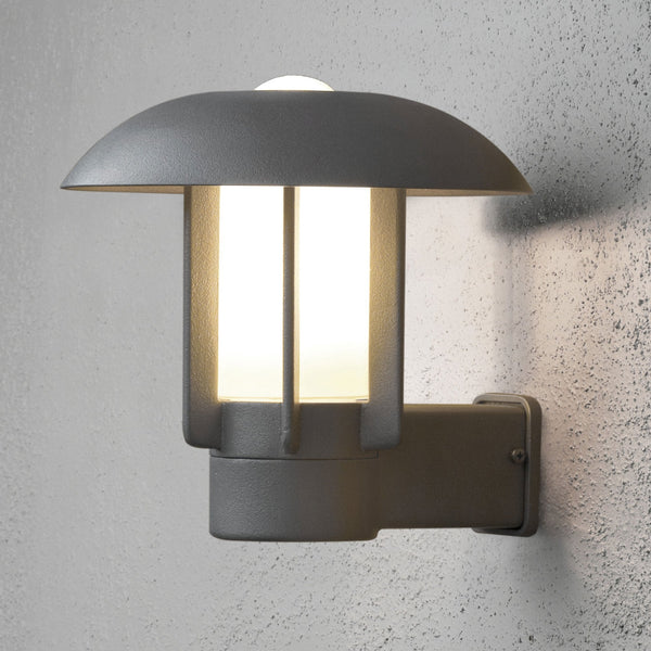 A modern outdoor wall light with a grey finish and a mushroom-shaped top, illuminating a textured wall.