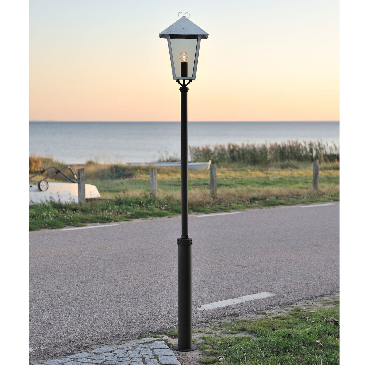 A classic lamp post stands by a coastal road with the sea in the background.
