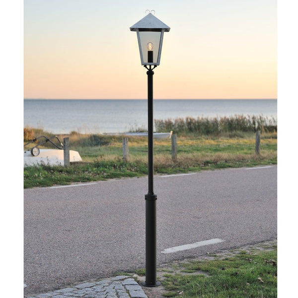 A classic lamp post stands by a coastal road with the sea in the background.