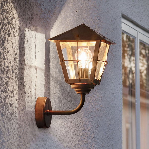 A close-up of a bronze outdoor wall light with a clear glass shade, illuminating a wall.