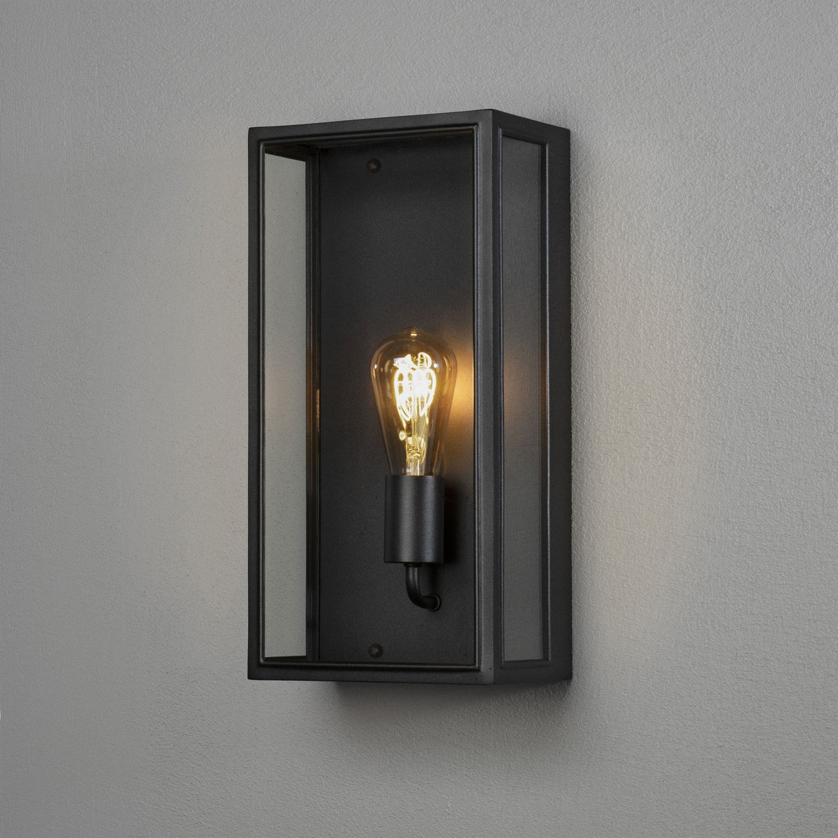 A close-up of a black rectangular outdoor wall light with an exposed Edison bulb.