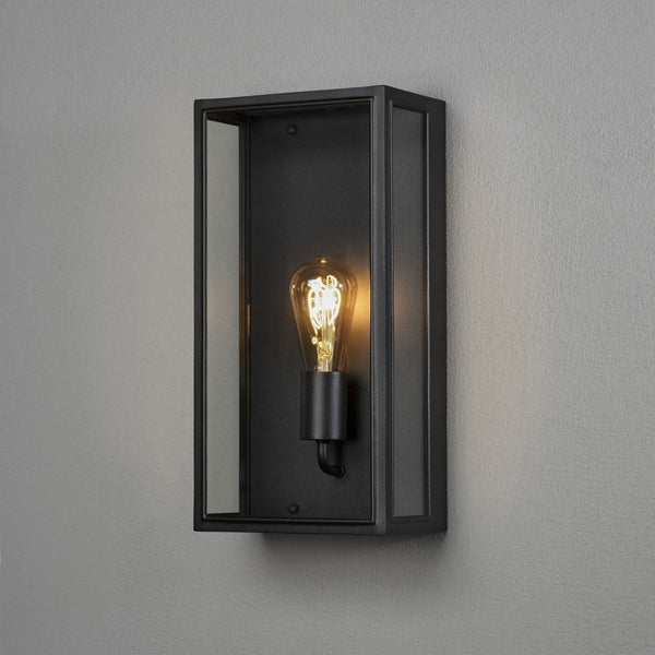 A close-up of a black rectangular outdoor wall light with an exposed Edison bulb.