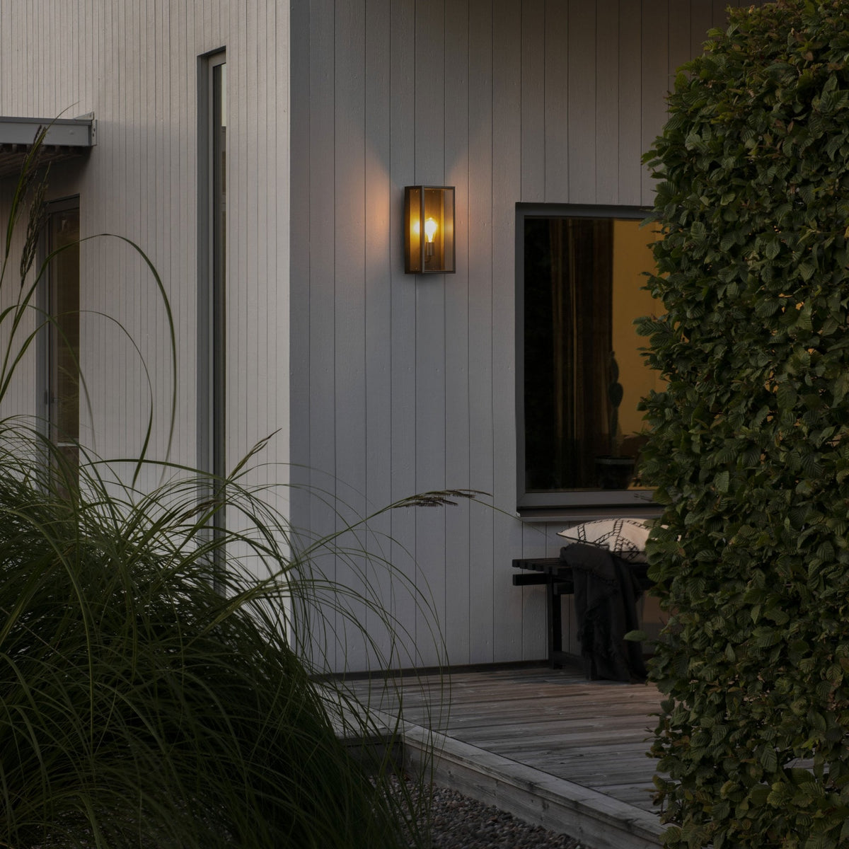 An outdoor wall light illuminating the side of a modern house with wooden cladding.