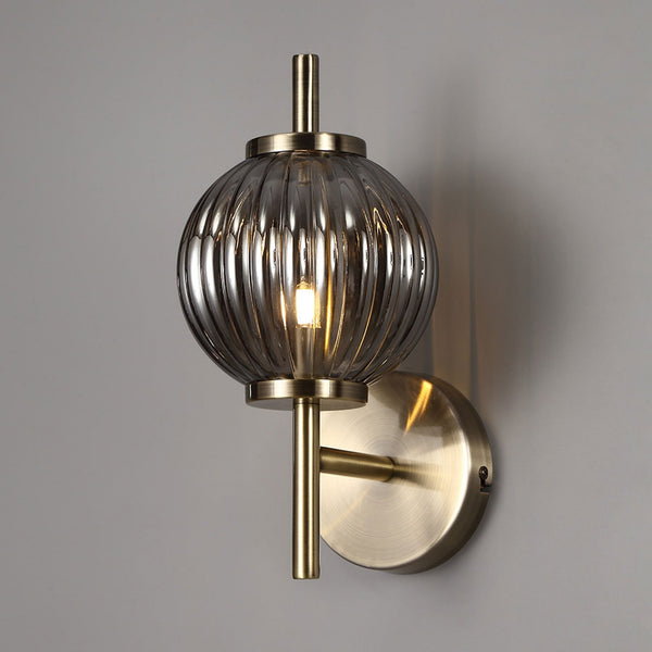 Wall-mounted light fixture with glass shade and brass finish on a gray background