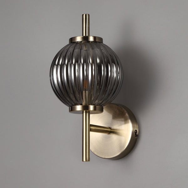 Ribbed smoked glass wall light with antique brass fittings on a grey wall.