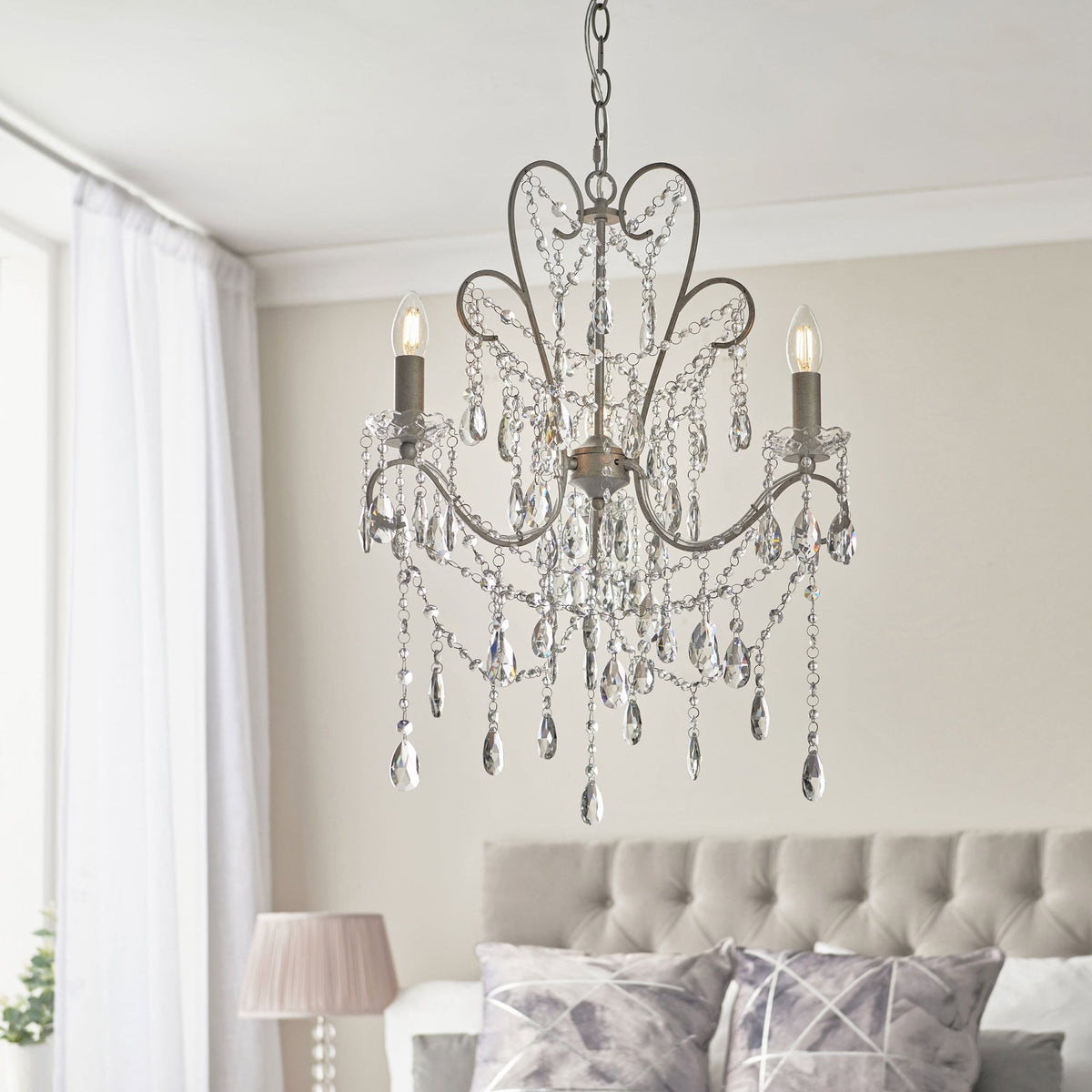 A two-light chandelier with crystal accents hangs above a bed with a tufted headboard.