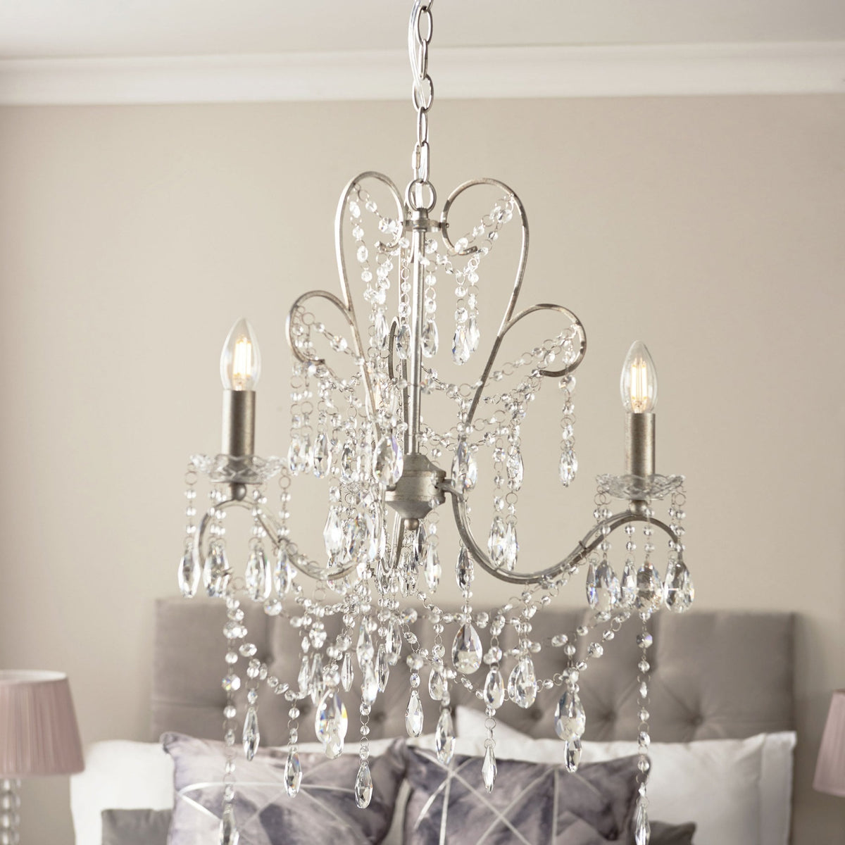 A two-light chandelier with crystal accents hangs above a bed with a tufted headboard and patterned pillows.