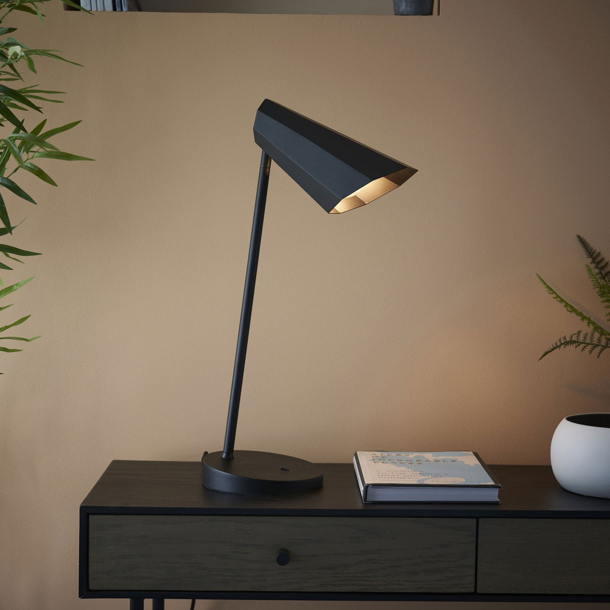 Black desk lamp with a geometric shade on a dark wooden console table.
