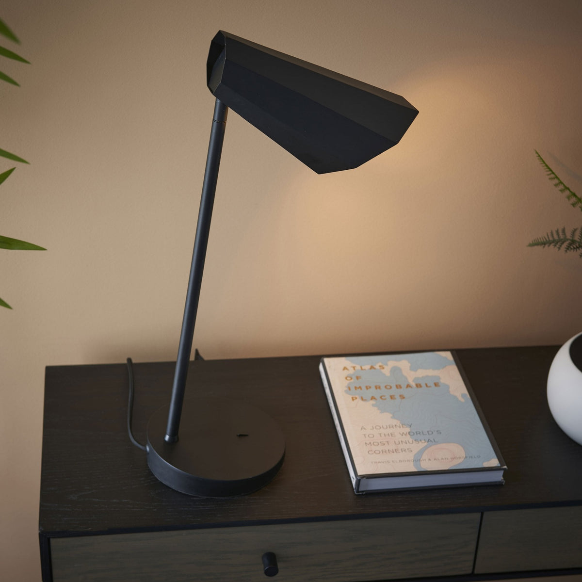 Black geometric desk lamp illuminating a book on a dark wooden console table.