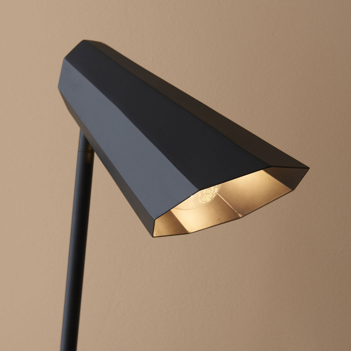 Close-up of the illuminated interior of a black geometric desk lamp shade.