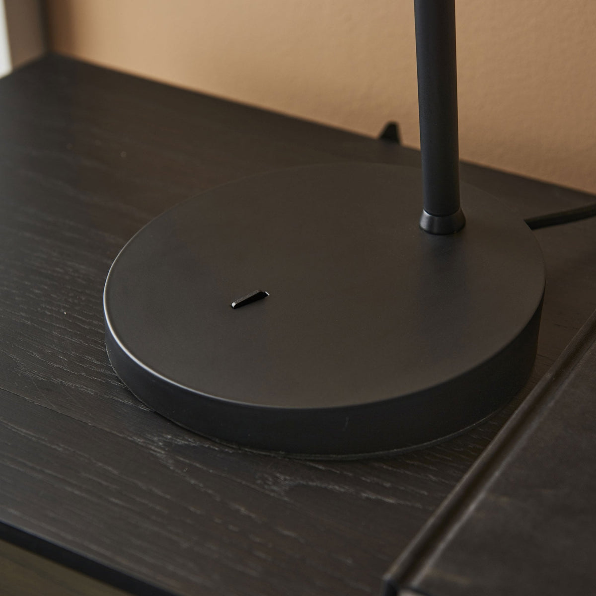 Close-up of the round black base of a desk lamp on a dark wooden surface.