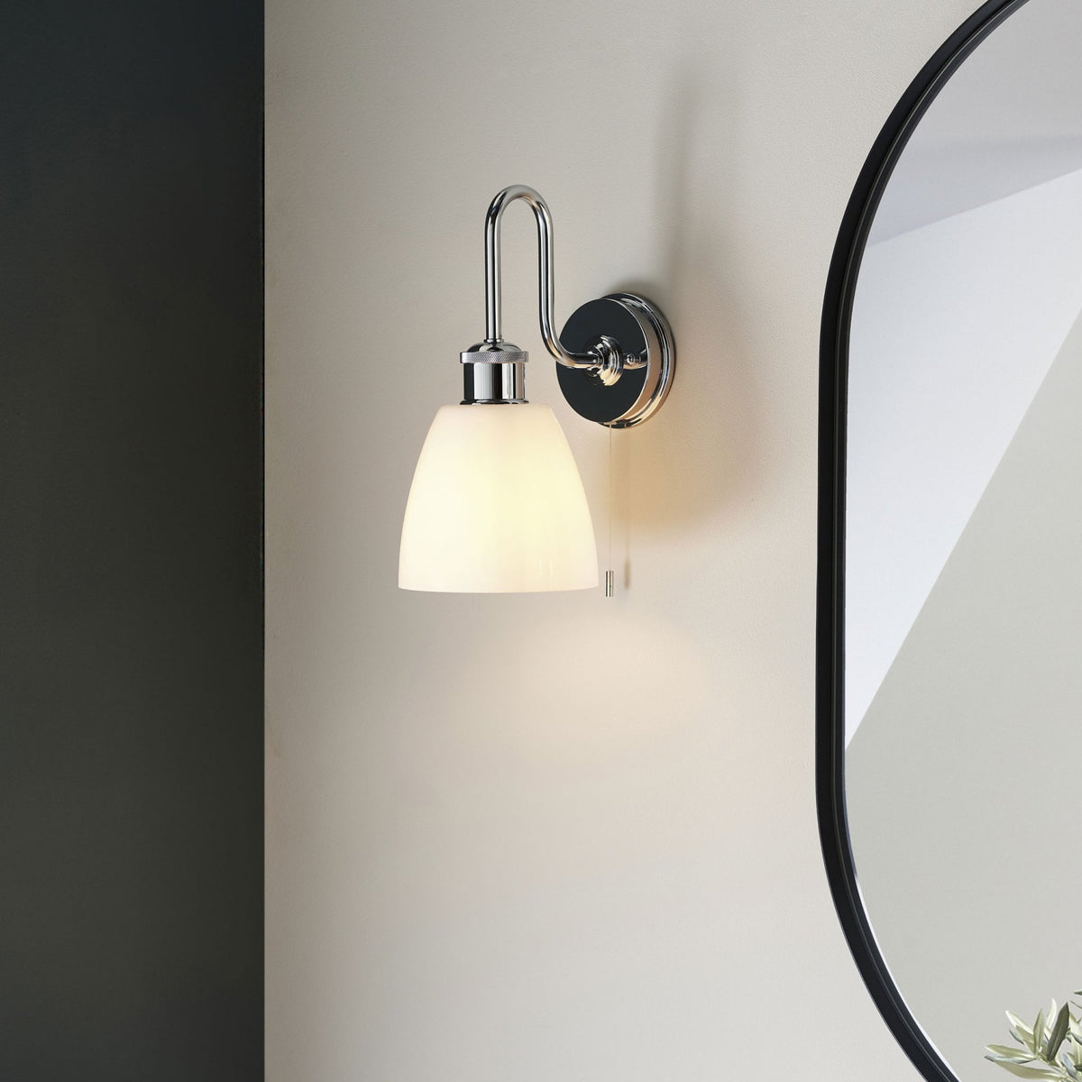 Chrome wall light with a white bell-shaped shade, casting a warm glow on a light-colored wall.