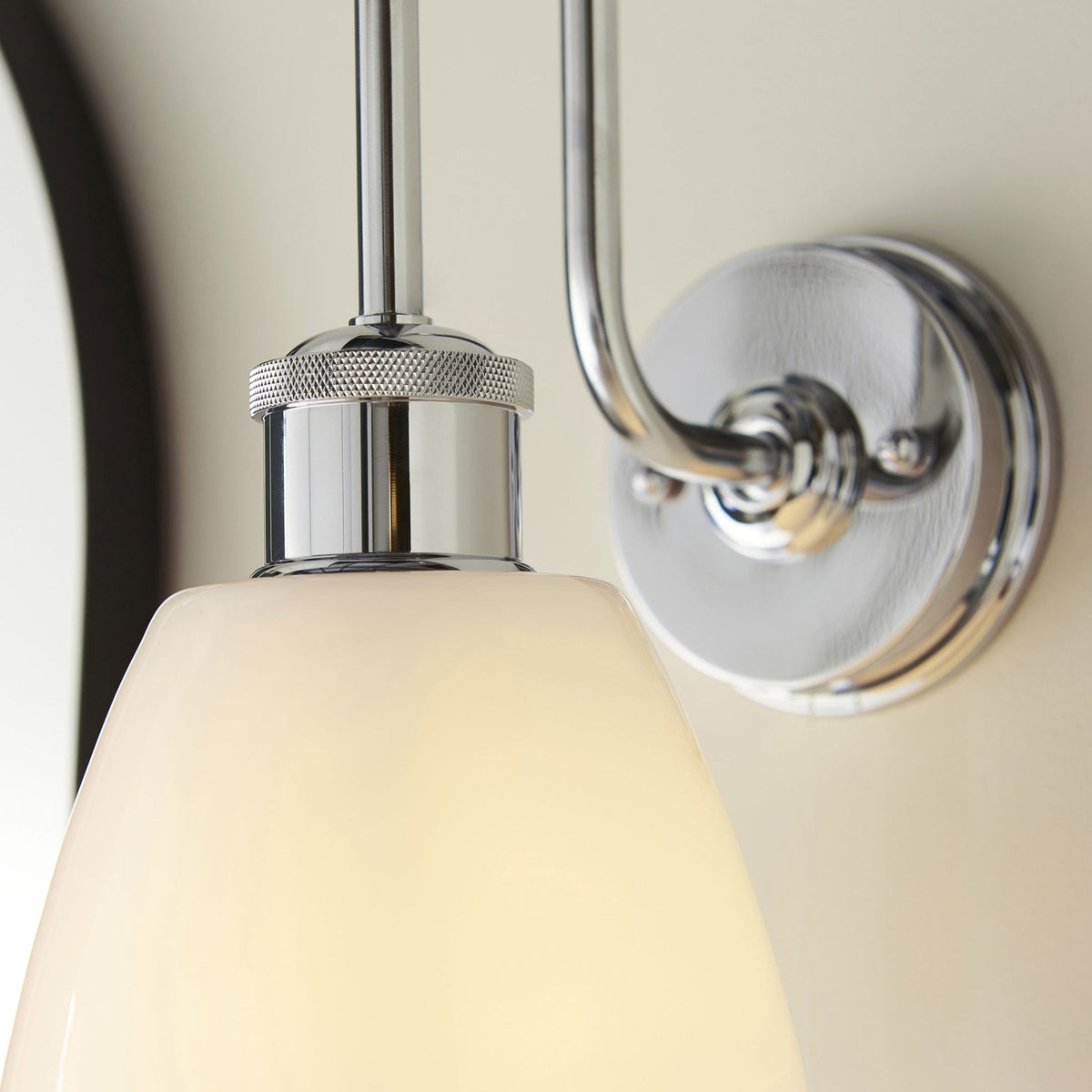 Close-up of a chrome wall light with a white shade, showing the textured detail on the fitting.