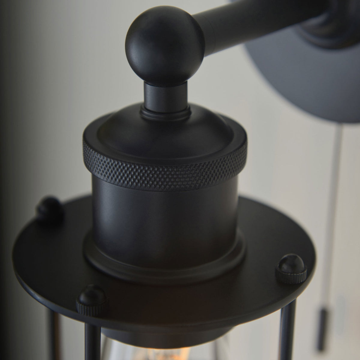 Close-up of the textured black metal details of a caged wall light, including the base and arm.
