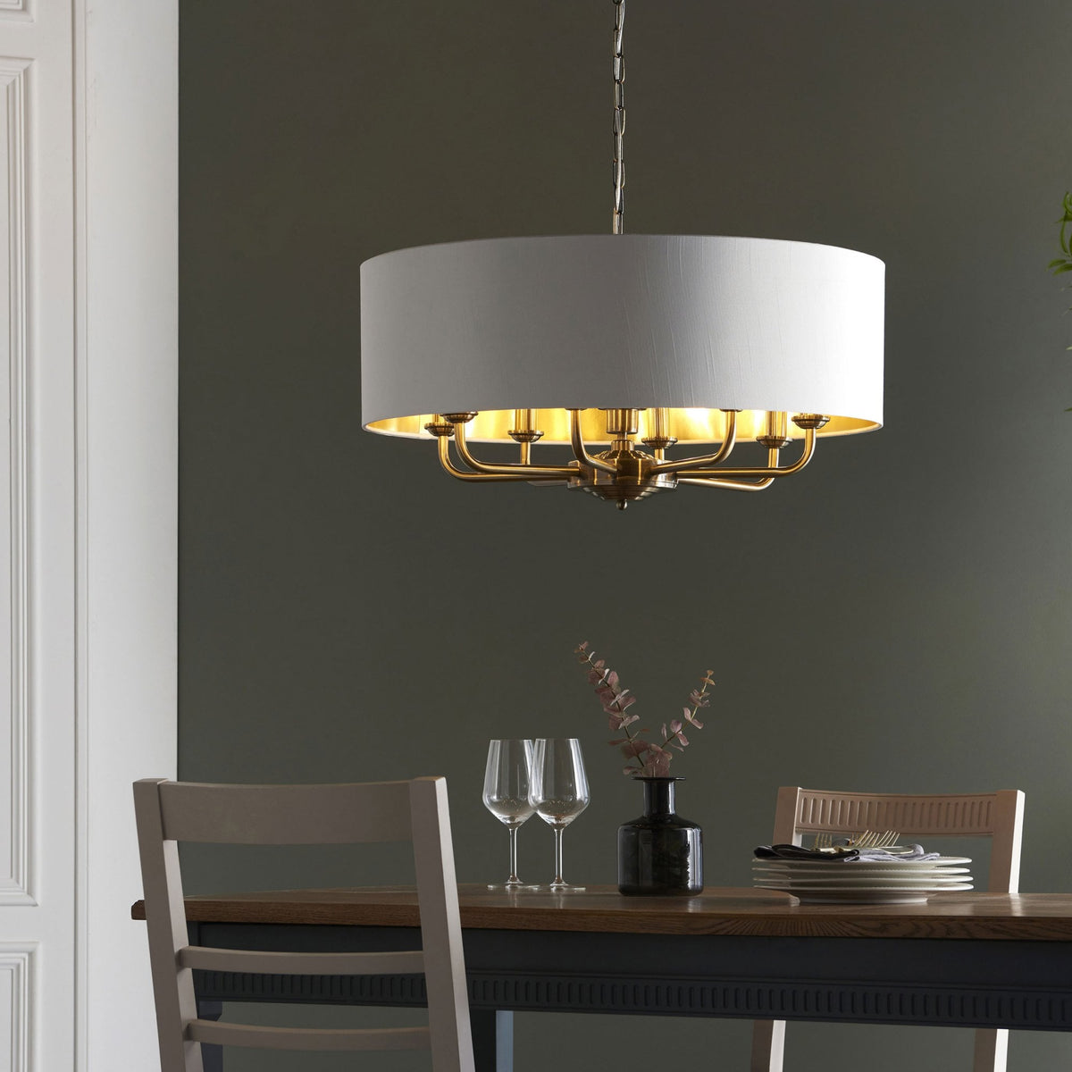A large, round pendant light with a white drum shade and brass interior hangs over a dining table.