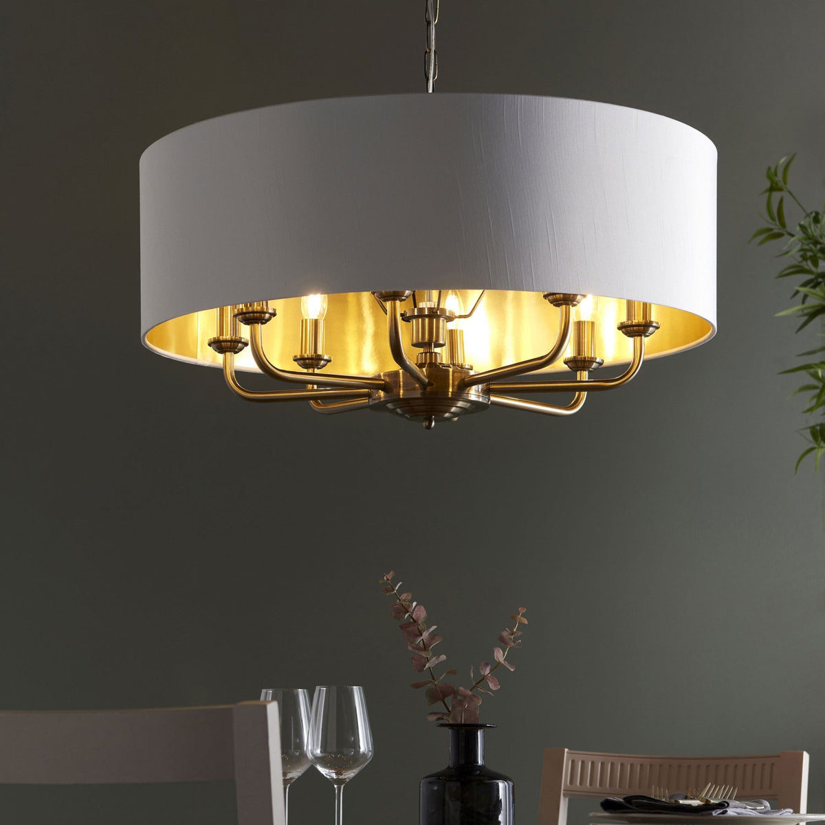 A large, round pendant light with a white drum shade and brass interior illuminates a dining area.