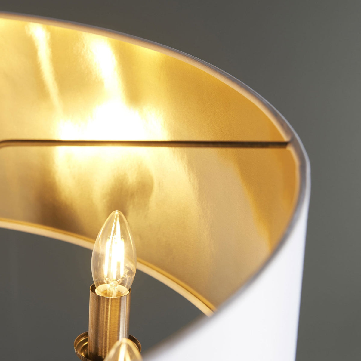 Close-up of a lit bulb and the golden interior of a white drum shade.
