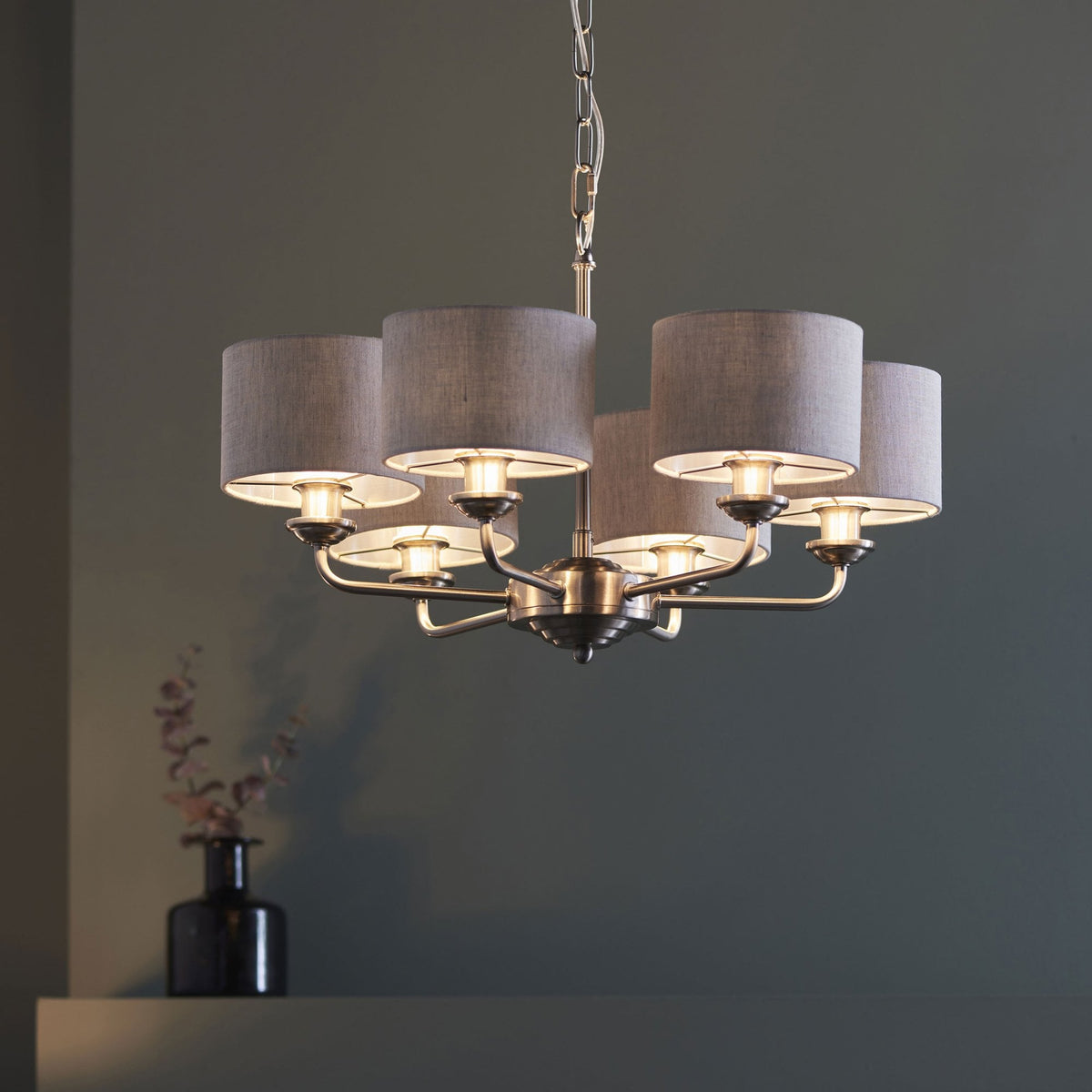 A five-light chandelier with grey fabric shades illuminates a dark green wall.