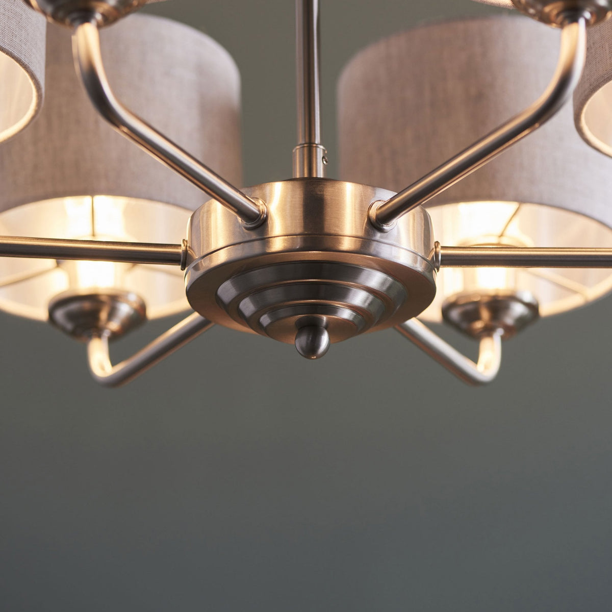 Close-up of the central column and arms of a five-light chandelier with grey fabric shades.