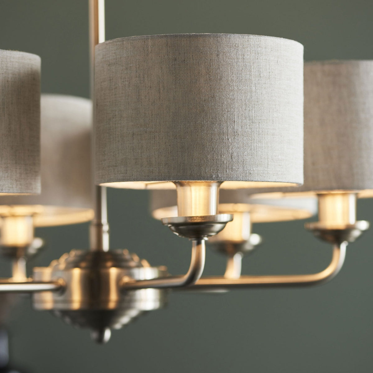 Close-up of a five-light chandelier with grey fabric shades, showing the warm light from the bulbs.