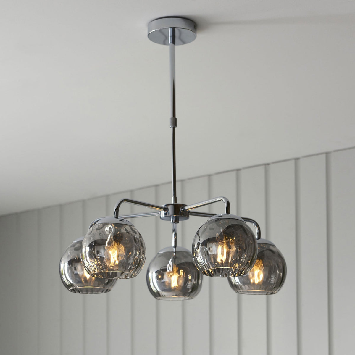 A chrome ceiling light with five smoked glass orb shades, illuminating a room with warm light.