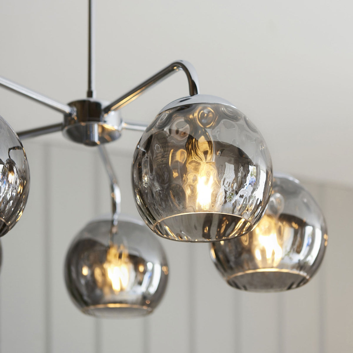 Close-up of a chrome ceiling light with five smoked glass orb shades, showing the textured glass and warm glow.