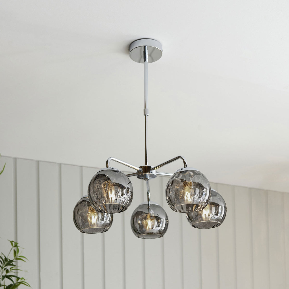A chrome ceiling light with five smoked glass orb shades, casting a warm glow in a modern room.