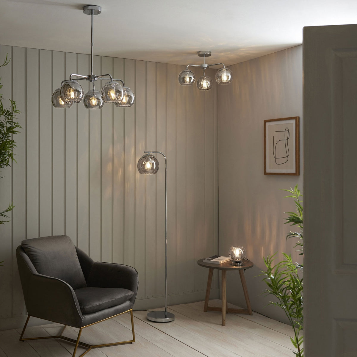 A modern living room with a chrome ceiling light, floor lamp, and table lamp, all with smoked glass shades.
