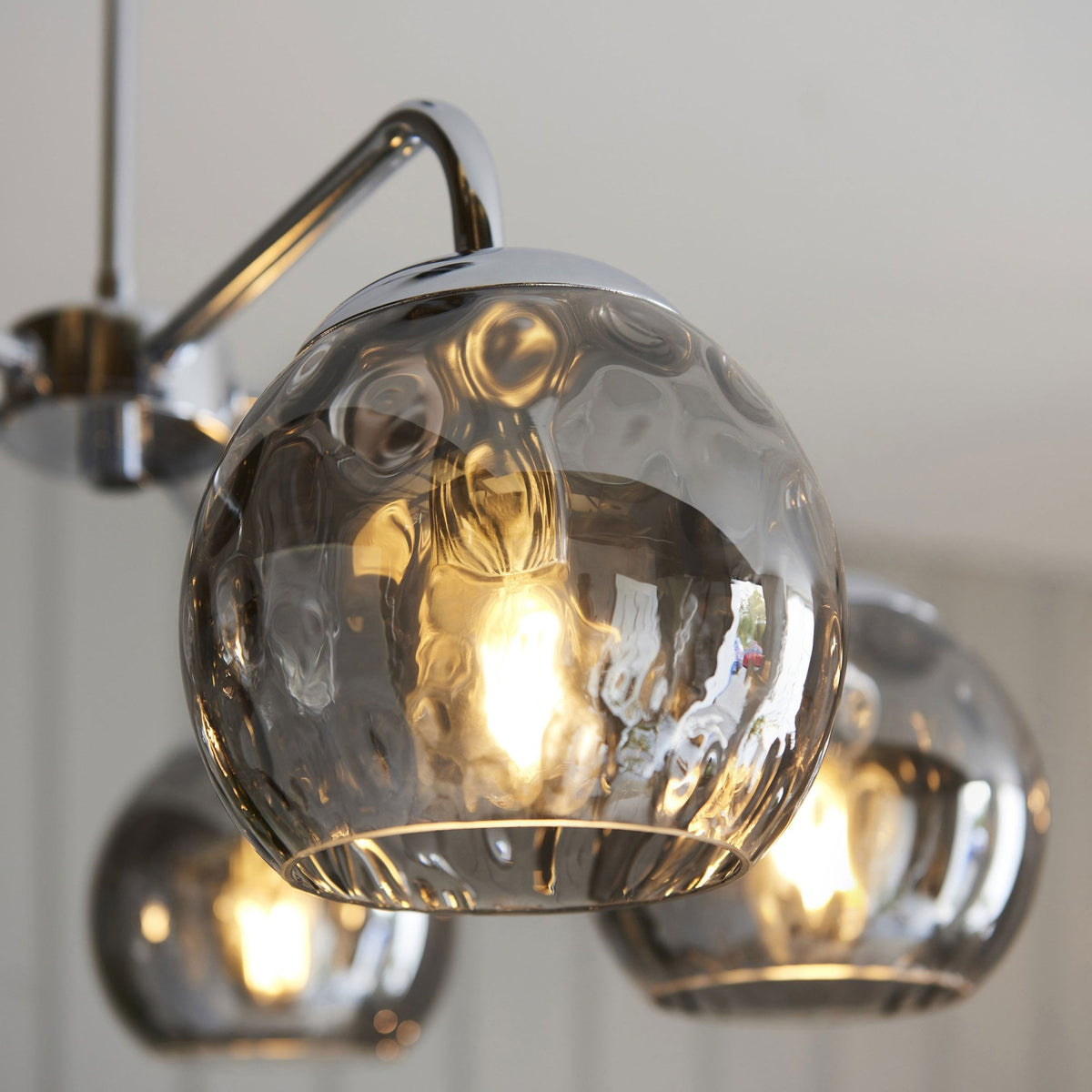 Close-up of a single smoked, textured glass orb shade on a chrome ceiling light, showing the illuminated bulb.
